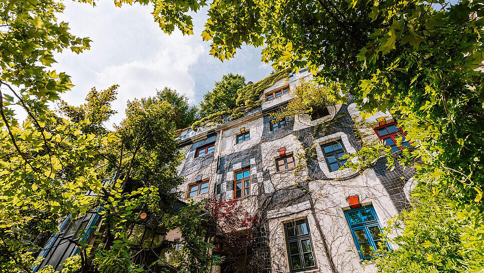 Hundertwasserhaus in Wien, bunte Fassade, davor üppig grüne Bäume