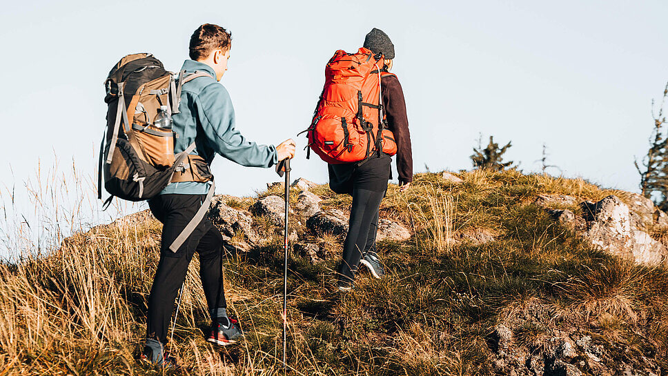 Zwei Menschen mit Trekkingrucksäcken, von hinten fotografiert, die in den Bergen wandern