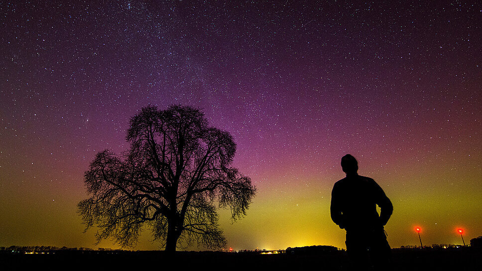 Mensch beobachtet Polarlichter am Nachthimmel in Brandenburg
