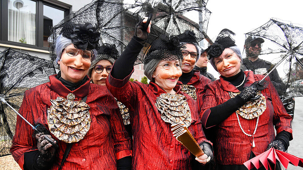 Eine Gruppe rot gekleideter Frauen mit Greis:innenmasken und Schirmen