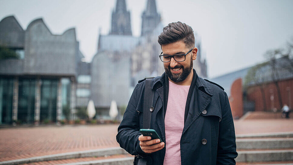 Ein Mann schaut aufs Smartphone, im Hintergrund der Kölner Dom