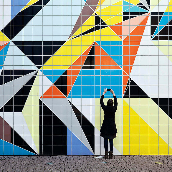 Eine Frau fotografiert das bunte Fliesen-Mosaik „Hornet“ von der Künstlerin Sarah Morris