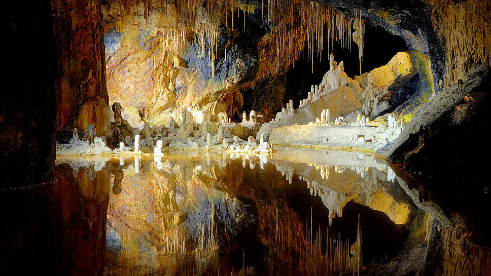 Beleuchtete Höhle. Stalaktiten und Stalagmiten spiegeln sich im Wasser. 