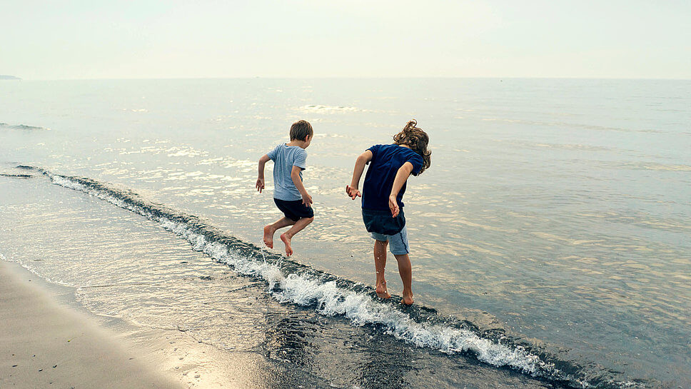 Zwei Kinder springen am Stand über die Wellen.