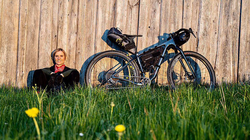 Sara Hallbauer auf einer Wiese auf dem Boden sitzend, neben ihrem Fahrrad